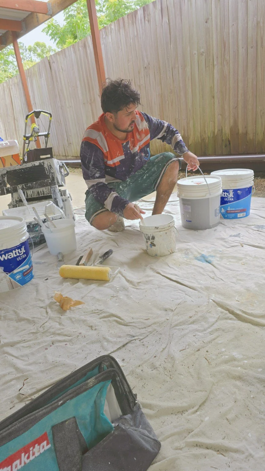 Painter preparing paint beside buckets and rollers on protective drop sheets